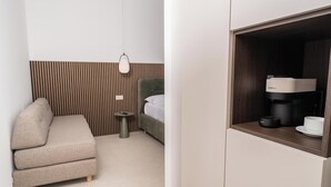 A modern hotel room with a sofa, a small round table, a bed, and a coffee machine. - Ypnos Rooms (Naples)