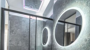 A modern bathroom with a glass-enclosed shower, a round mirror, and a white sink on an orange countertop. - Ypnos Rooms (Naples)