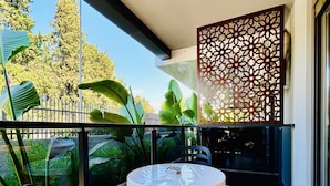 Un balcón con una mesa redonda y sillas, un separador decorativo y vistas a la vegetación y árboles.