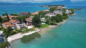 An aerial view of a coastal town with buildings along the waterfront, a clear blue sea, and mountains in the background. - Villa Canneto dep.Smeraldo (Sirmione)