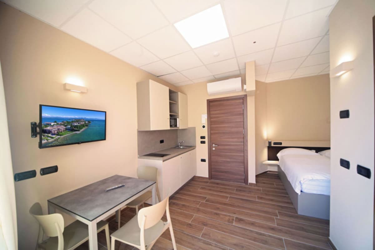 A compact hotel room with a kitchenette, a dining area, a bed, and a television mounted on the wall.