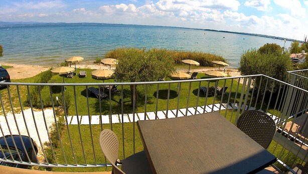 A balcony with a view of a lake, outdoor seating with umbrellas, and a table. - Villa Canneto dep.Smeraldo (Sirmione)
