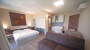 A modern hotel room with a bed, a sofa, a kitchenette, and a bathroom. - Villa Canneto dep.Smeraldo (Sirmione)