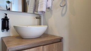 A bathroom with a white vessel sink on a wooden vanity, a black soap dispenser, and a towel rack with towels. - w Marvelous Loft w Modern Deco in Bogota (Bogotá)