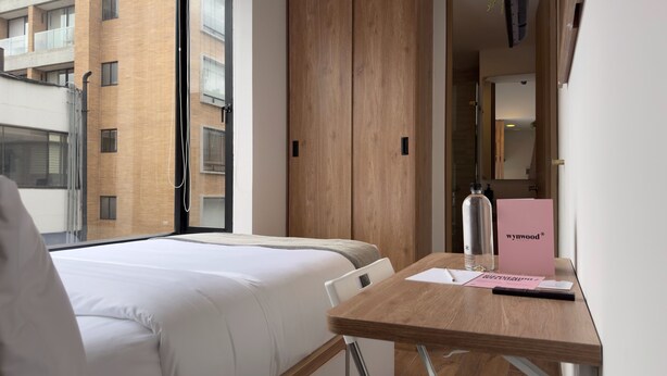 A hotel room with a bed, a wooden desk, and a window with a view of a brick building. - w Marvelous Loft w Modern Deco in Bogota (Bogotá)