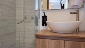 A bathroom with a large white vessel sink, a wooden vanity, a glass shower enclosure, and a wall-mounted soap dispenser. - w Marvelous Loft w Modern Deco in Bogota (Bogotá)
