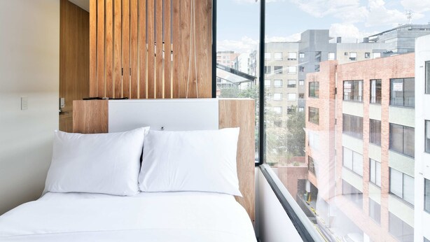 A modern hotel room with a large bed, wooden panel wall, and a view of the cityscape. - w Cozy Loft w Modern Deco in Bogota (Bogotá)