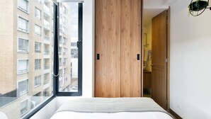 A modern bedroom with a large window, a wooden wardrobe, and a view of a building outside. - w Cozy Loft w Modern Deco in Bogota (Bogotá)