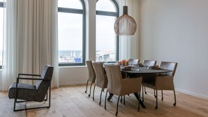 A dining area with a round table, six chairs, and a hanging light fixture. - Stunning Seafront Apartment With Modern Comforts and Dike Views (Ostend)