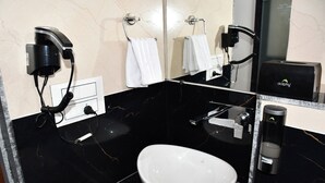 A modern bathroom with a black marble sink, a white basin, a hairdryer, and a towel rack. - Hotel RC Garh (Nathdwara)