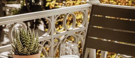 A table with a potted plant, a cup, and a book on a balcony with a railing.