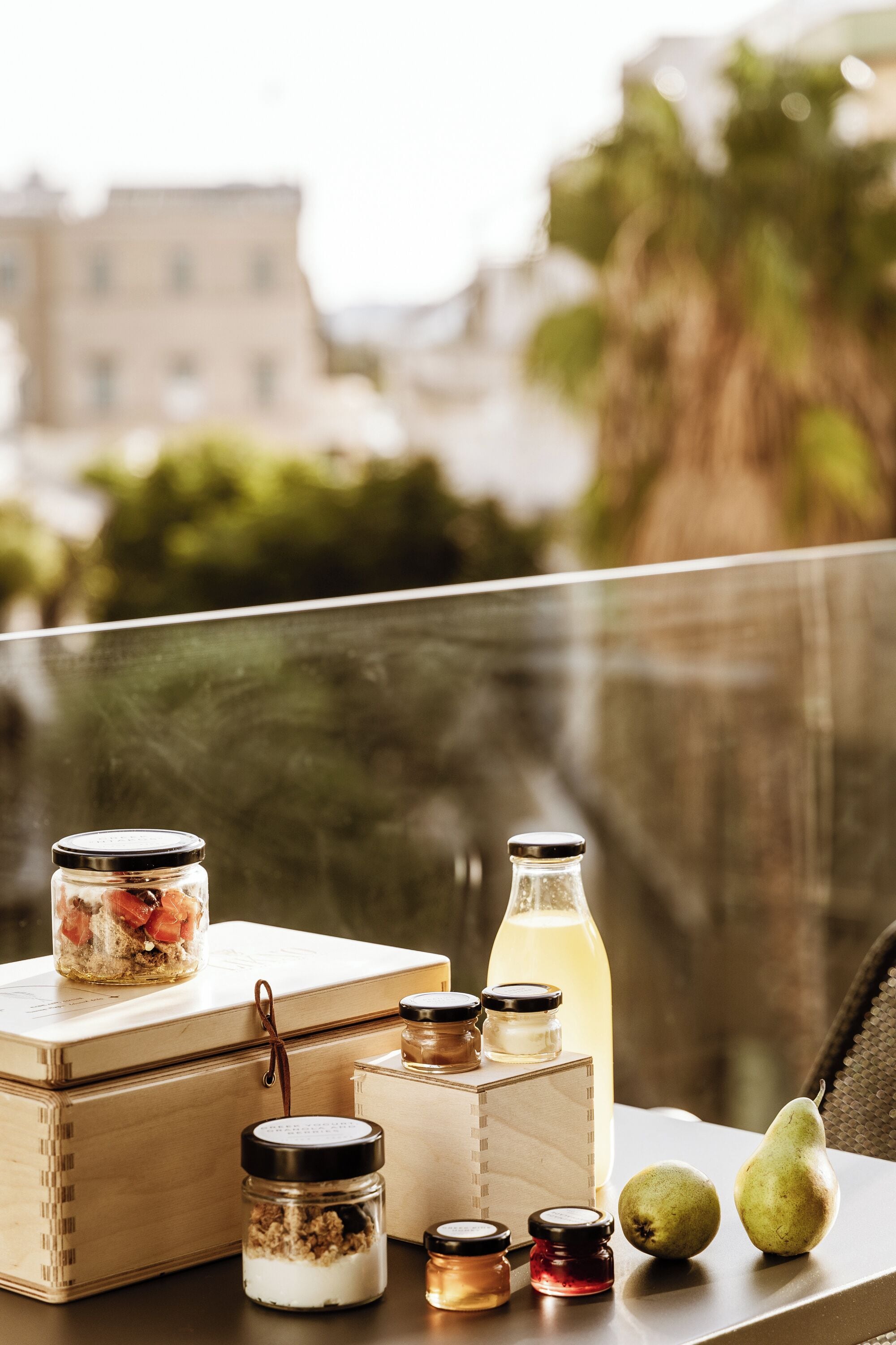 A wooden table with jars, a bottle, and pears on a balcony with a city view.