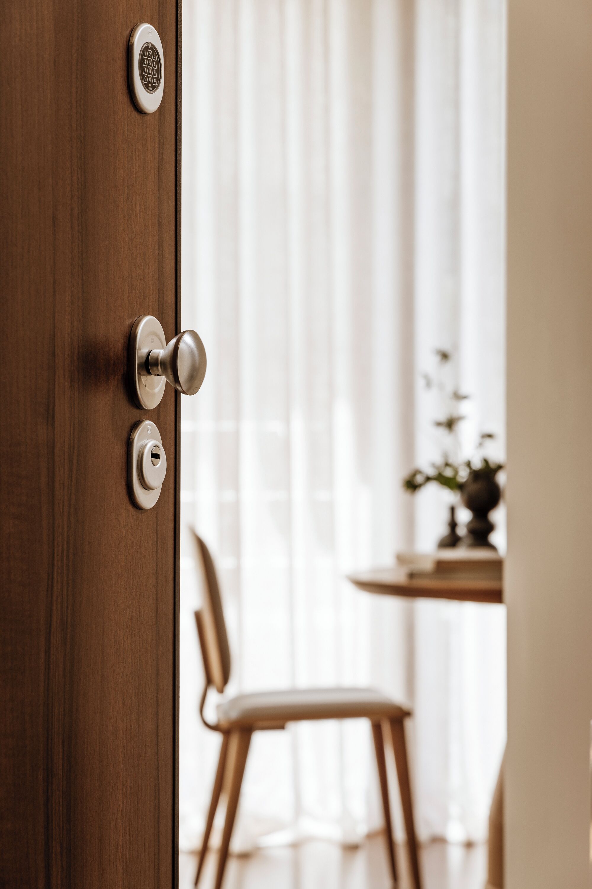 A wooden door with a modern lock and a keyhole, leading to a room with a dining table and chairs.