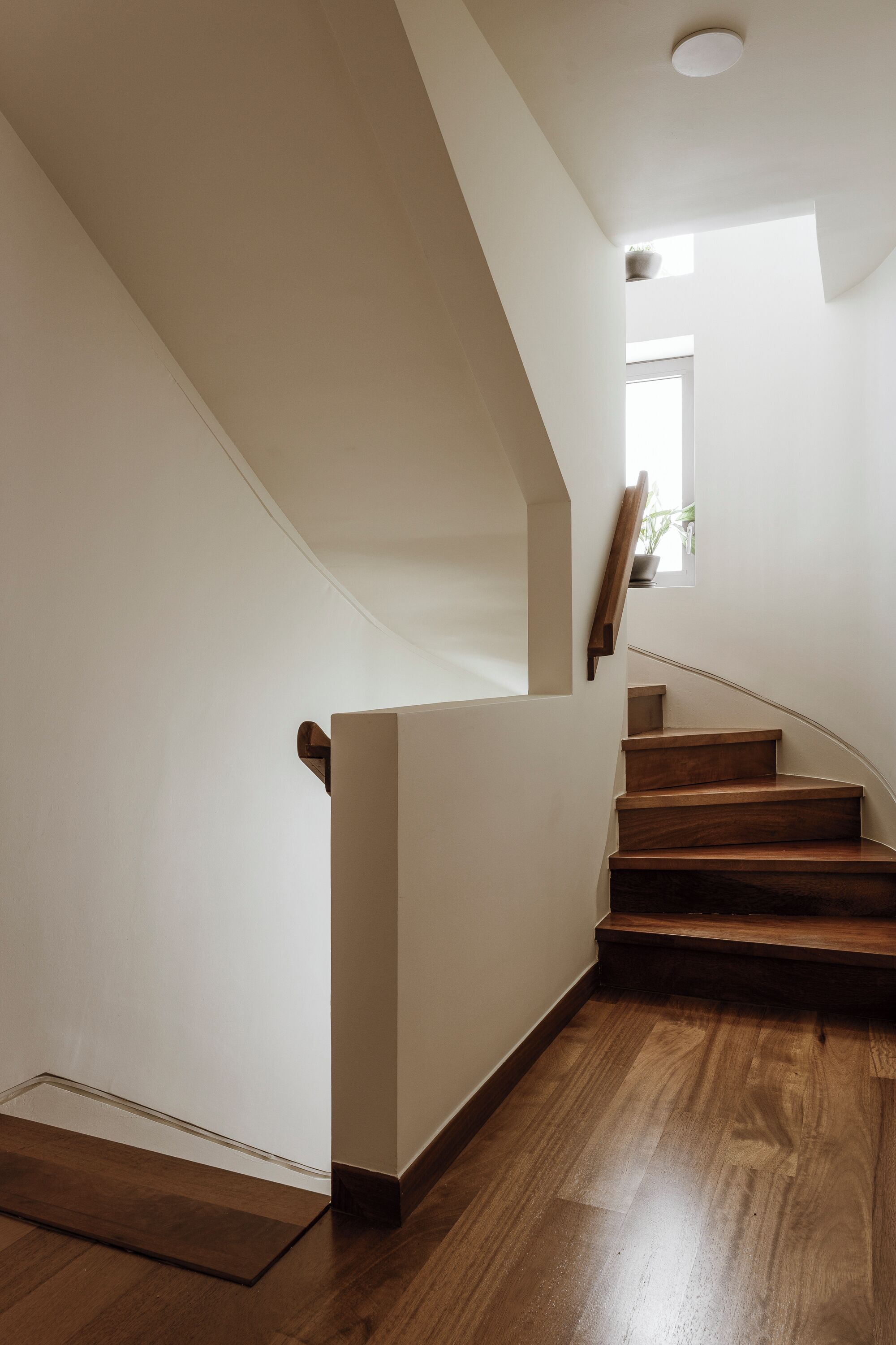 A staircase with wooden steps and a handrail, leading to a landing with a small window.