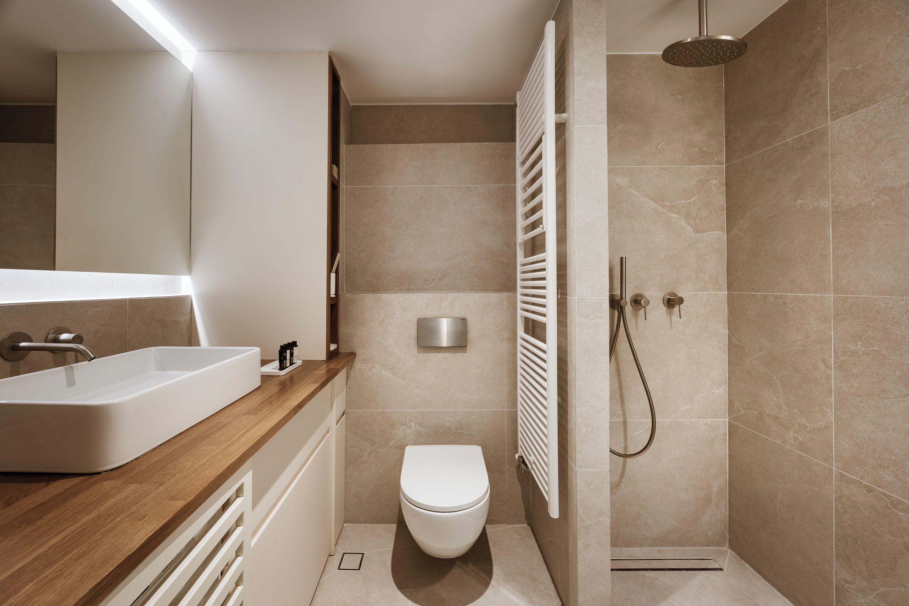 Une salle de bain moderne avec un meuble-lavabo en bois, un lavabo blanc, des toilettes et une douche équipée d’un porte-serviettes blanc.
