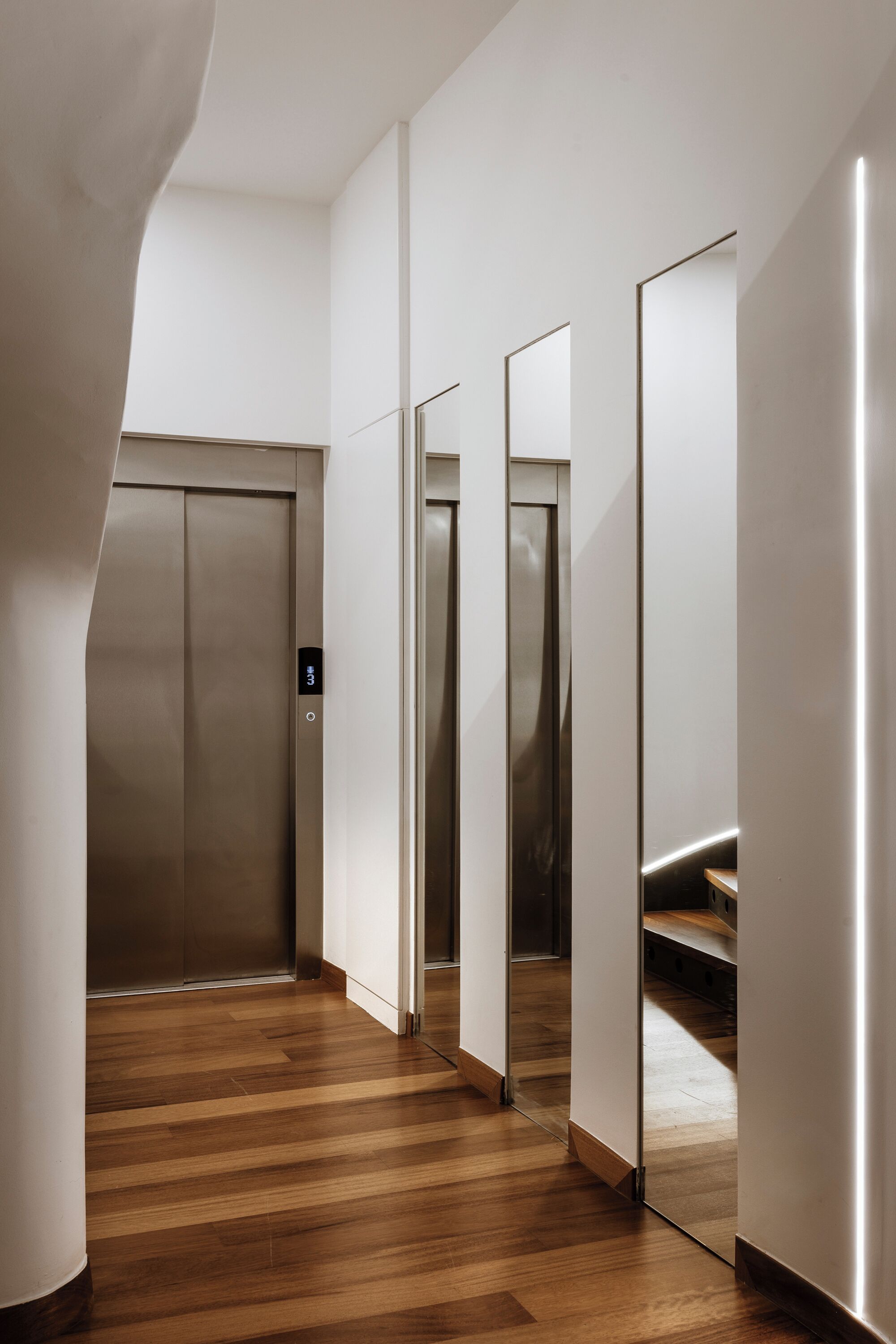 A modern elevator area with a wooden floor and a mirrored wall.