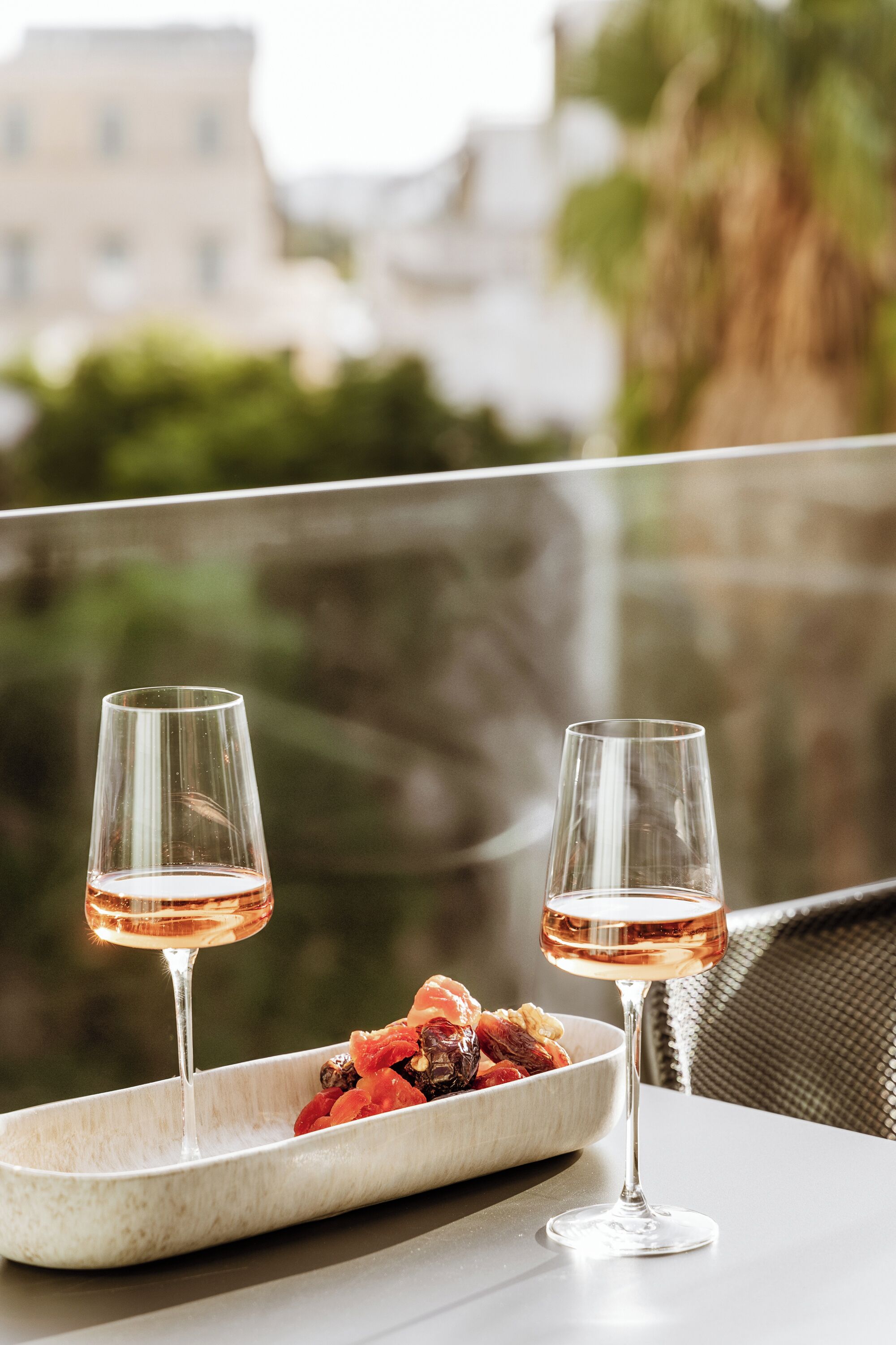 Zwei Gläser Roséwein auf einem Tisch mit einer Schüssel Früchte und Nüssen.