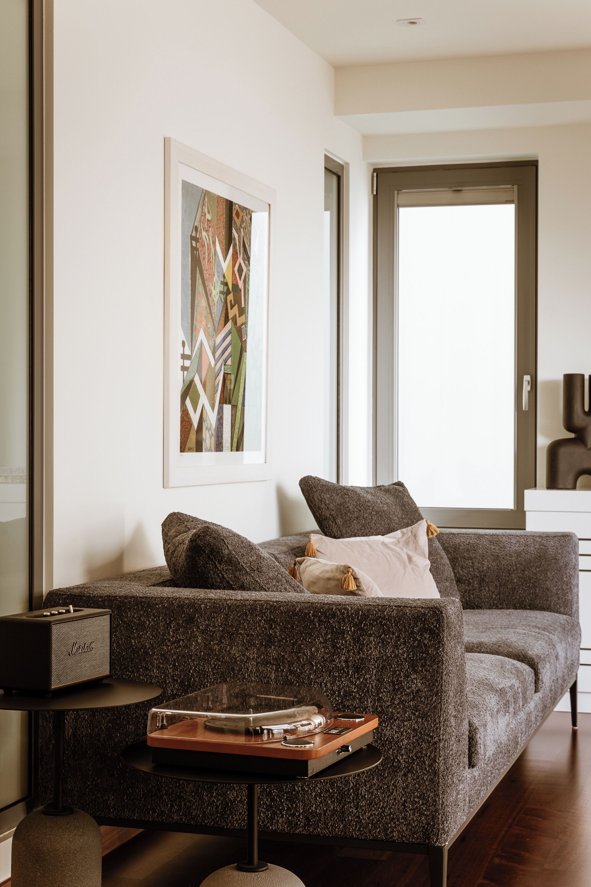 Un soggiorno moderno con un divano grigio, un tavolino con un giradischi e un quadro astratto incorniciato appeso al muro.
