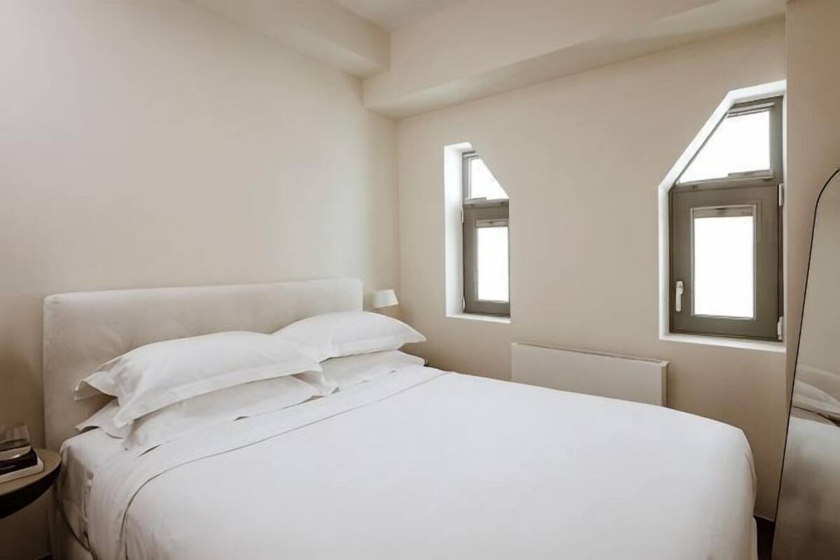 A bedroom with a bed, two windows, and a nightstand.