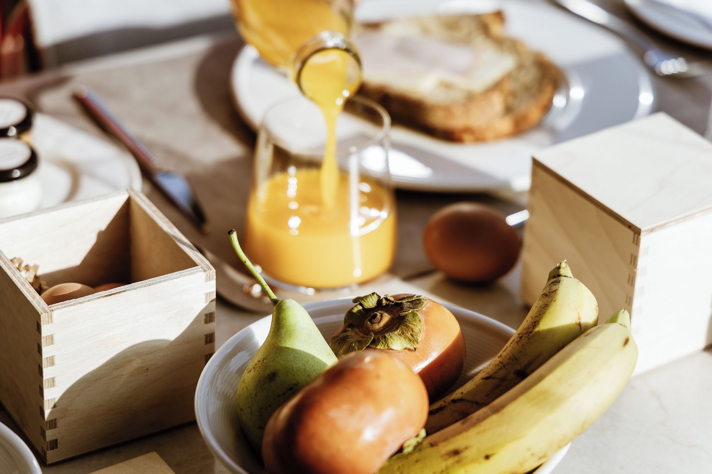 A breakfast setting with a wooden crate, a plate with a pear, an onion, and bananas, and a glass of orange juice.