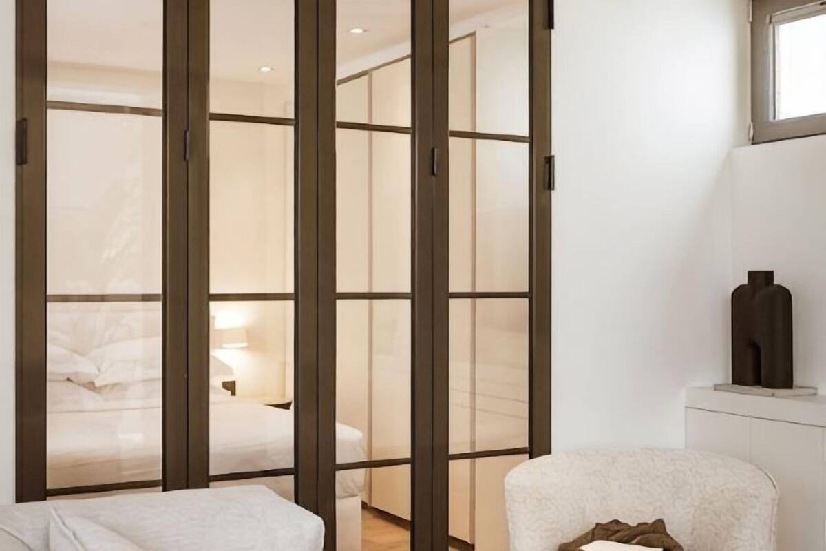 A hotel room with a sliding door leading to a bedroom, a bedside table, and a window.