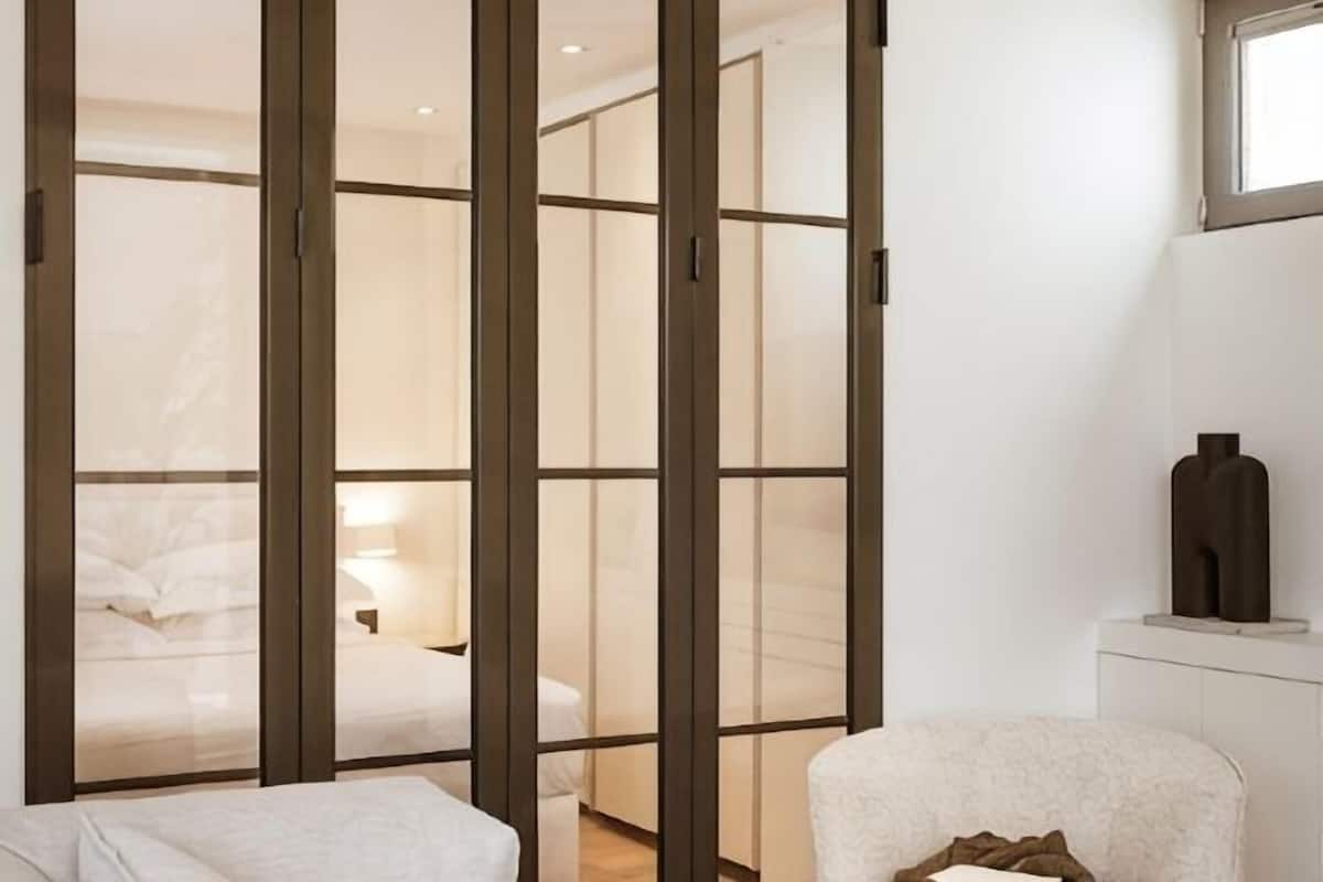 A hotel room with a sliding door leading to a bedroom, a bedside table, and a window.