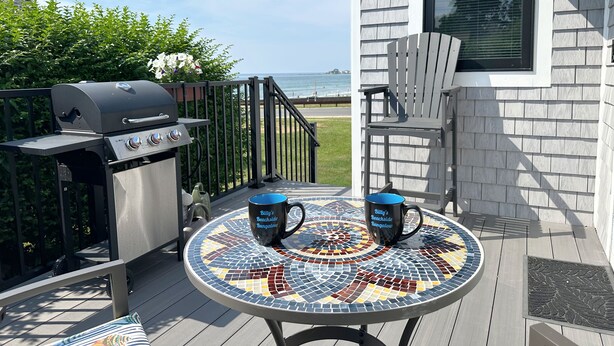 A patio with a grill, two mugs, a chair, and a view of the ocean. - Billy's Beachside Bungalow - near Wallis Sands Beach (Rye)