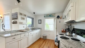 A modern kitchen with white cabinets, granite countertops, a stainless steel stove, and a window with blinds. - Billy's Beachside Bungalow - near Wallis Sands Beach (Rye)