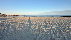 A wide sandy beach with footprints leading towards the water, a clear sky, and a distant shoreline with buildings. - Billy's Beachside Bungalow - near Wallis Sands Beach (Rye)