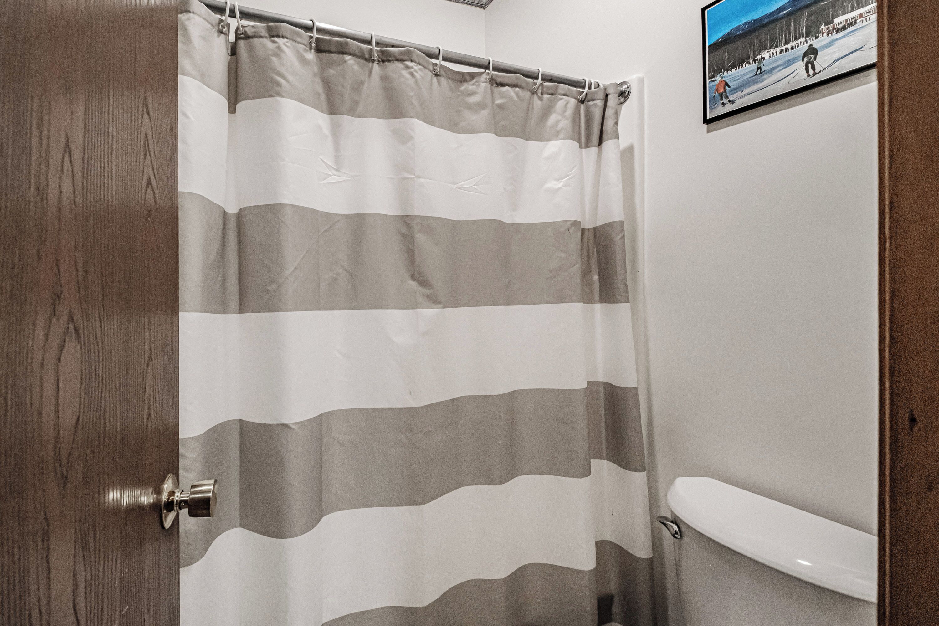 A bathroom with a striped shower curtain, a toilet, and a framed picture on the wall.