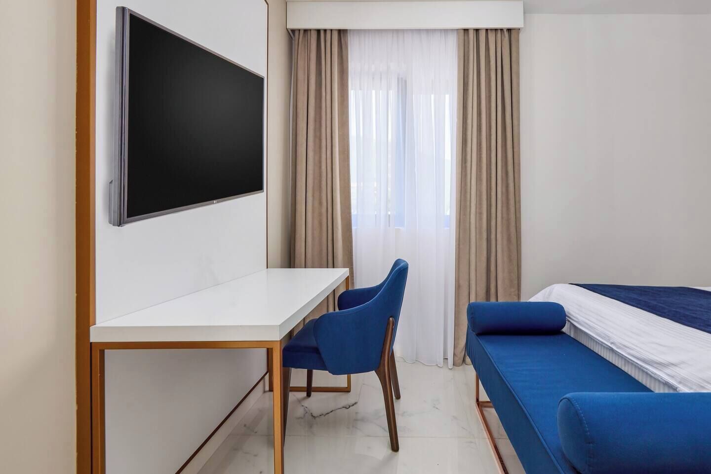Quarto de hotel com cama, escrivaninha e cadeira.