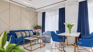 A modern living room with a blue sofa, a coffee table, a patterned armchair, and a dining table with blue chairs. - Moderna Luxury Apartments-One bedroom with terrace 2

 (Tivat)