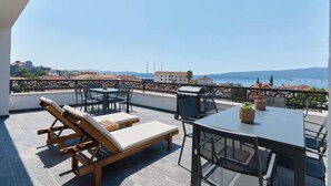 A terrace with a table and chairs, a grill, and a view of the sea and buildings. - Moderna Luxury Apartments-One bedroom with terrace 2

 (Tivat)