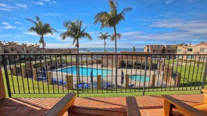 Un área de piscina con vista al océano, rodeada de palmeras y una valla.