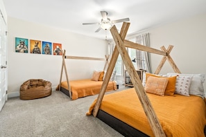 Un dormitorio con cama, sillón de mimbre, ventilador de techo y cuadros en la pared.