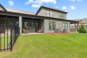 A modern two-story house with a covered patio, outdoor seating, and a well-maintained lawn.