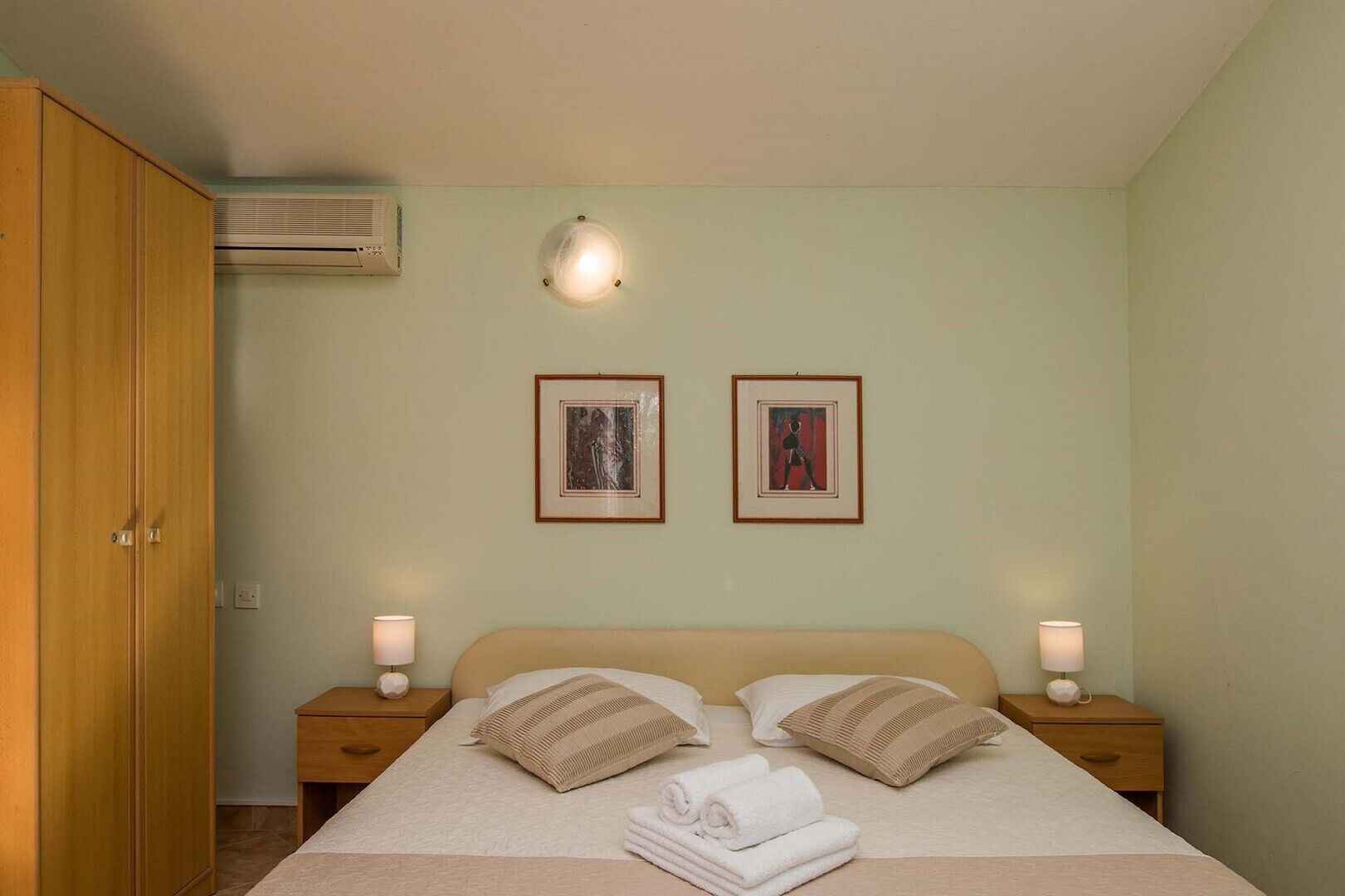 A bedroom with a bed, two bedside tables, a wardrobe, and two framed pictures on the wall.