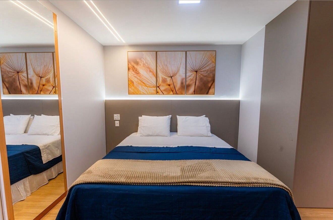 A modern bedroom with a large bed, a headboard with built-in lighting, and a wall-mounted artwork above the bed.
