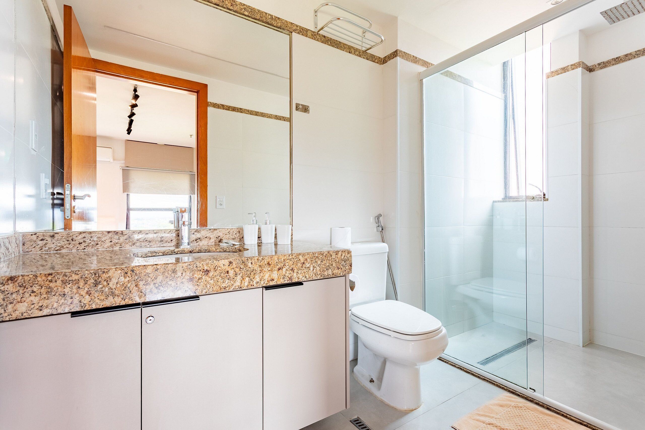 Et moderne badeværelse med bordplade i granit, glasvæg omkring brusebad og et hvidt toilet.