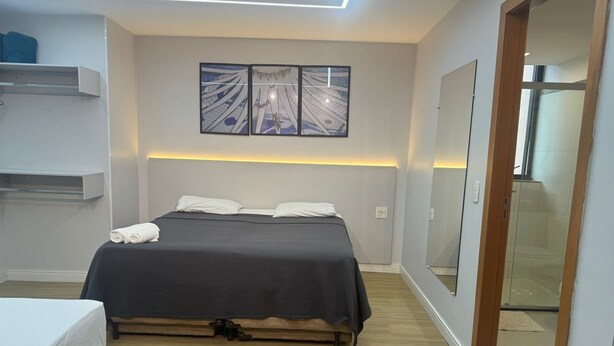 A modern bedroom with a bed, a bedside table, a wall-mounted shelf, and a large mirror.