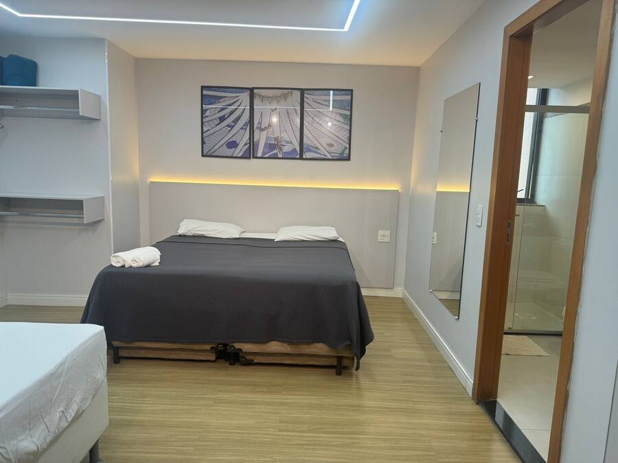 Quarto moderno com cama, mesa de cabeceira, prateleira na parede e um espelho grande.