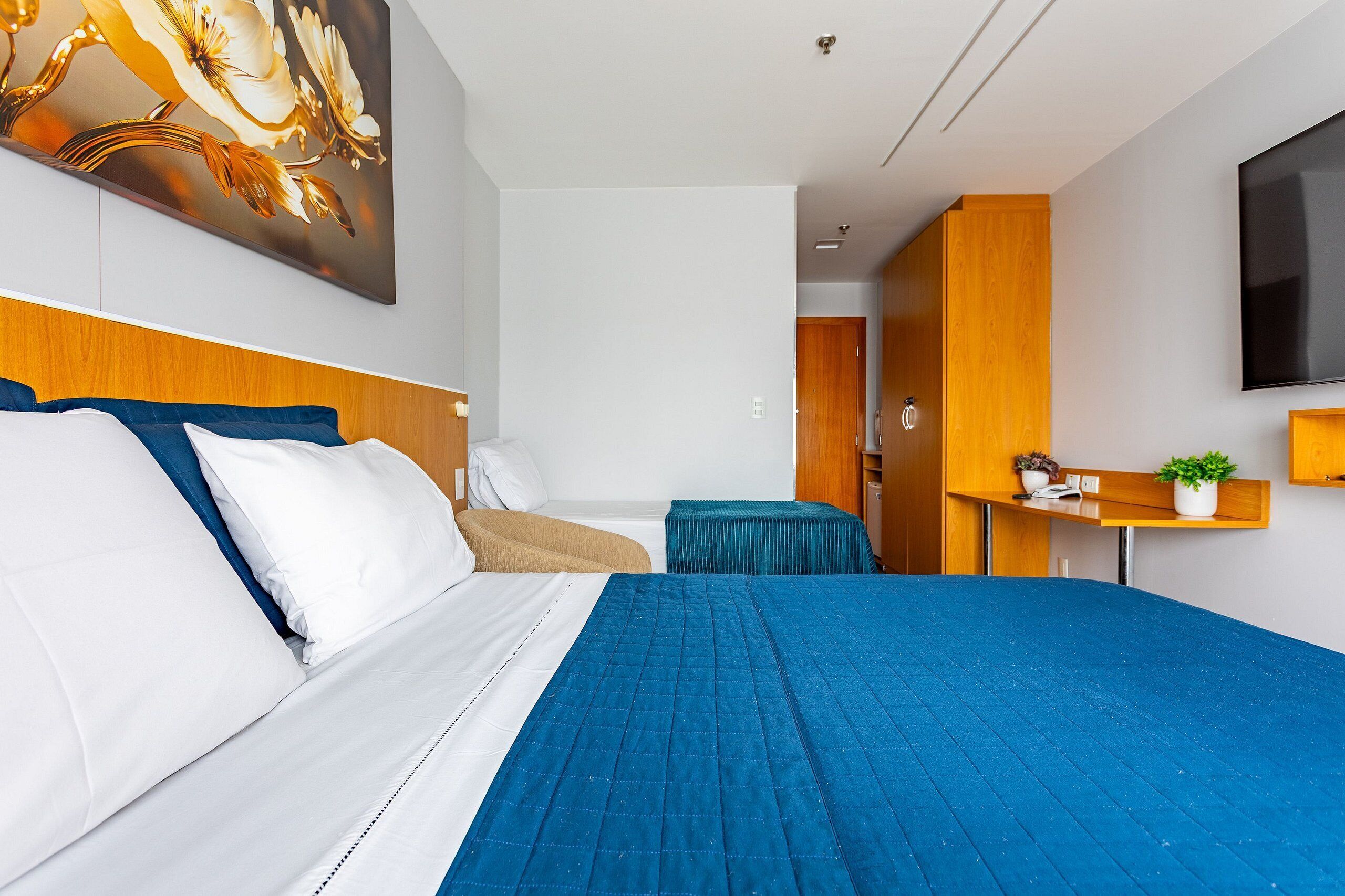 A hotel room with a large bed, a desk, a TV, and a painting on the wall.