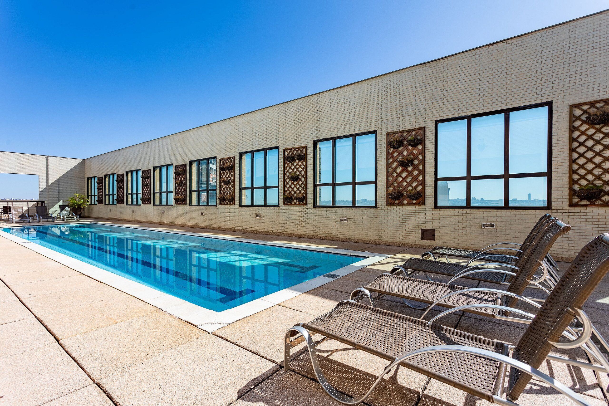 A swimming pool with lounge chairs and a brick building with large windows.