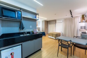 A modern kitchen with a microwave, refrigerator, and sink. There is a dining area with a table and chairs. - Apartamento no hotel Comfort (Taguatinga)