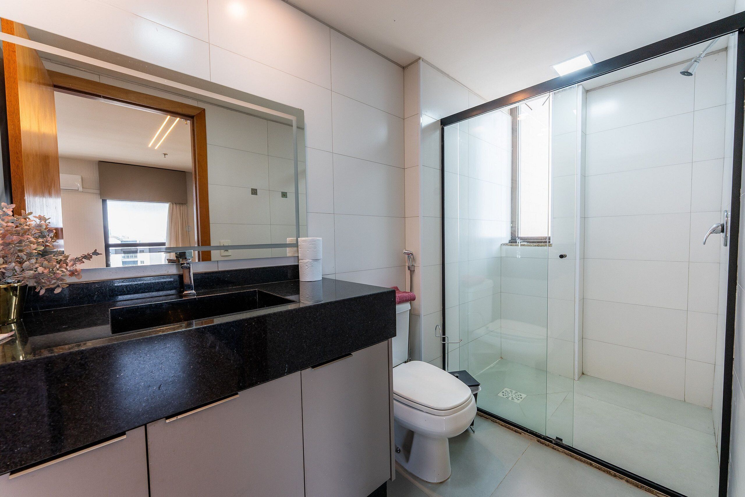 Ein modernes Badezimmer mit Duschkabine aus Glas, einer schwarzen Ablage und einer weißen Toilette.