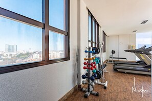 A gym with weightlifting equipment and treadmills, large windows, and a city view. - Apartamento no hotel Comfort (Taguatinga)