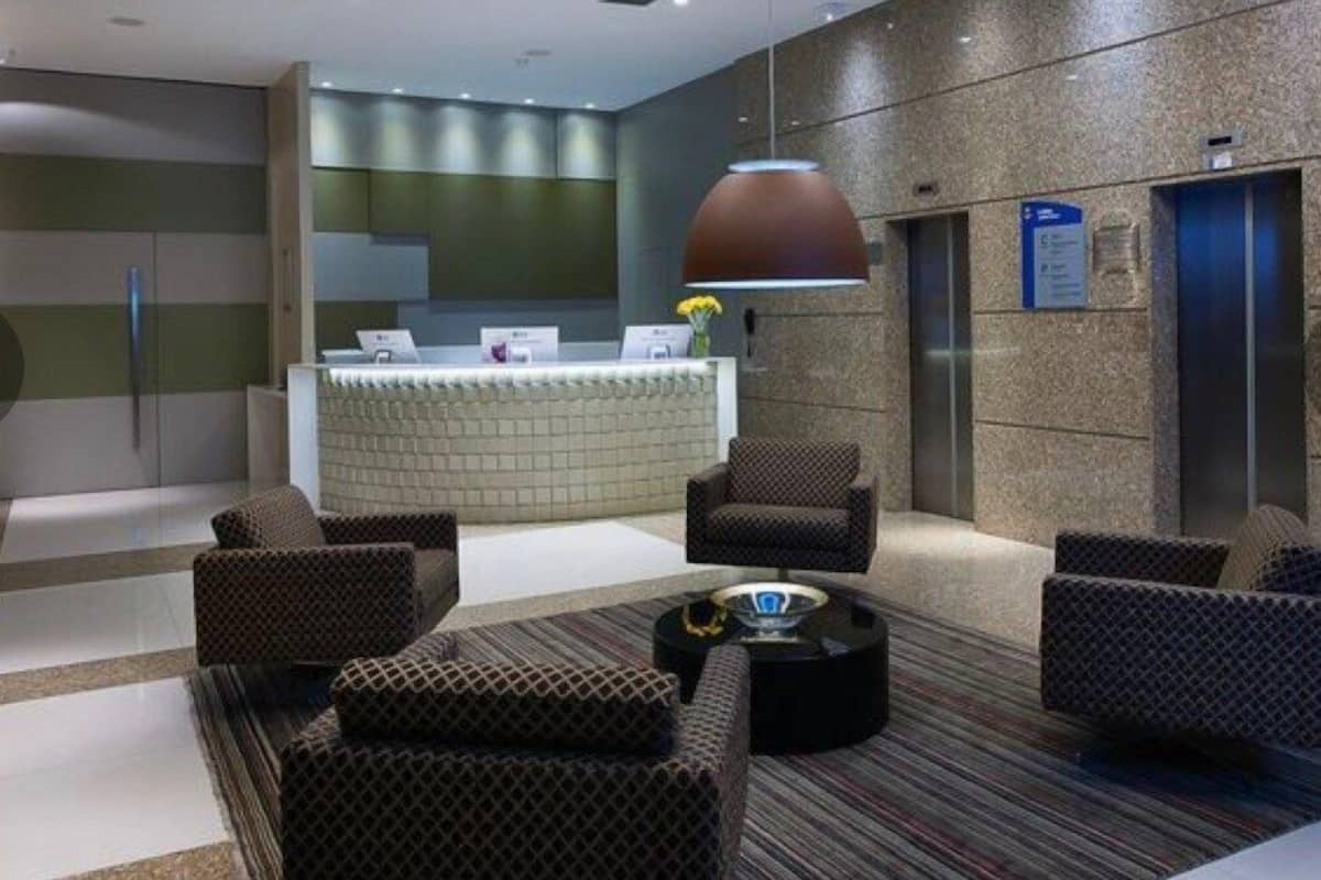 A modern lobby with a reception desk, seating area, and an elevator.