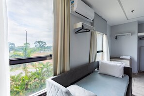 A hotel room with a bed, air conditioning unit, window with curtains, and a view of palm trees. - Apartamento no hotel Comfort (Taguatinga)