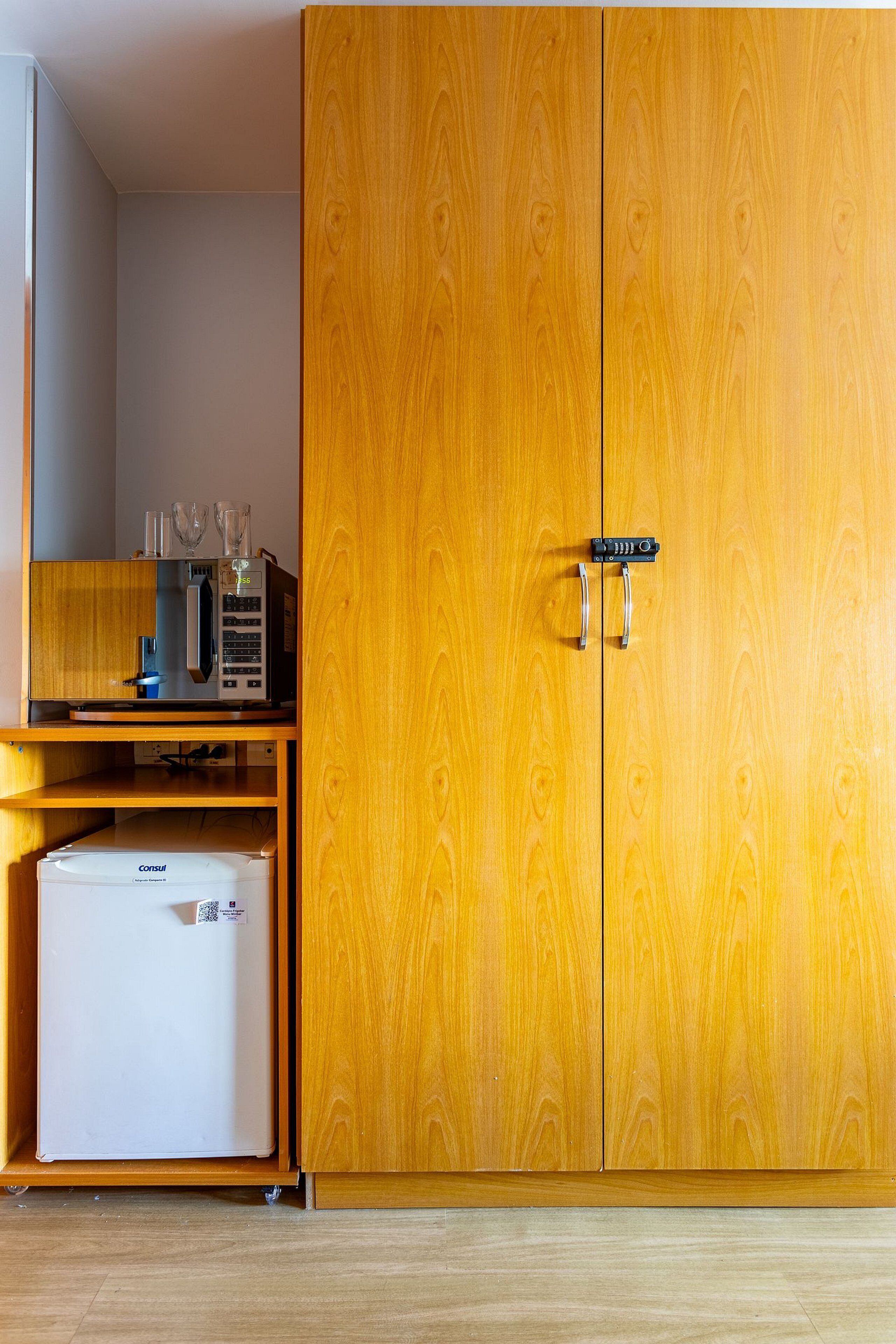 A wooden wardrobe with a microwave and a small refrigerator inside.