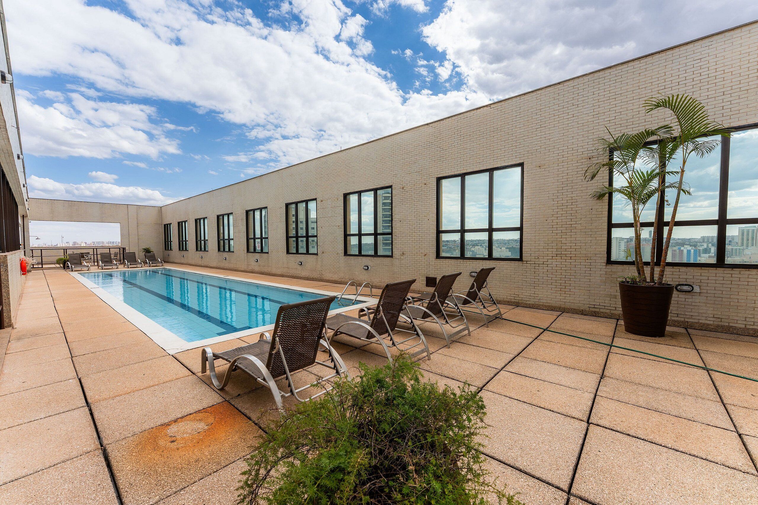 Uma piscina no terraço com vista clara para o horizonte da cidade, rodeada por um edifício de tijolo com grandes janelas e espreguiçadeiras.